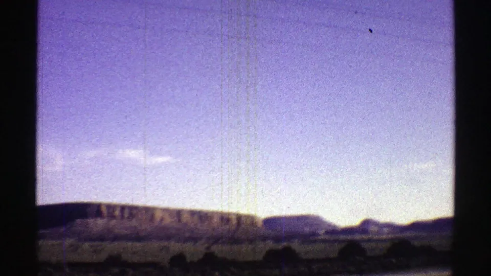 1969 Arizona countryside view with low hills, distant mountains, pale blue sky, and dark interior window framing.