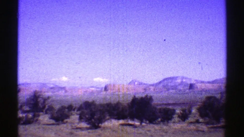 Faded 8mm frame of Arizona desert terrain with dark shrubs, distant mesas, and a color-shifted open sky.
