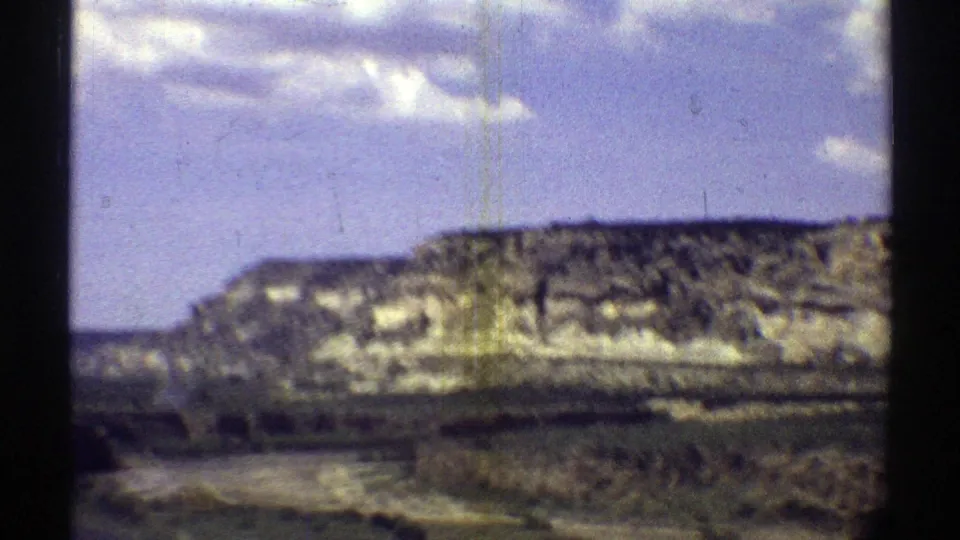 Arizona 8mm travel footage frame showing a rocky brown hillside, sparse vegetation, and clouds above the desert terrain.
