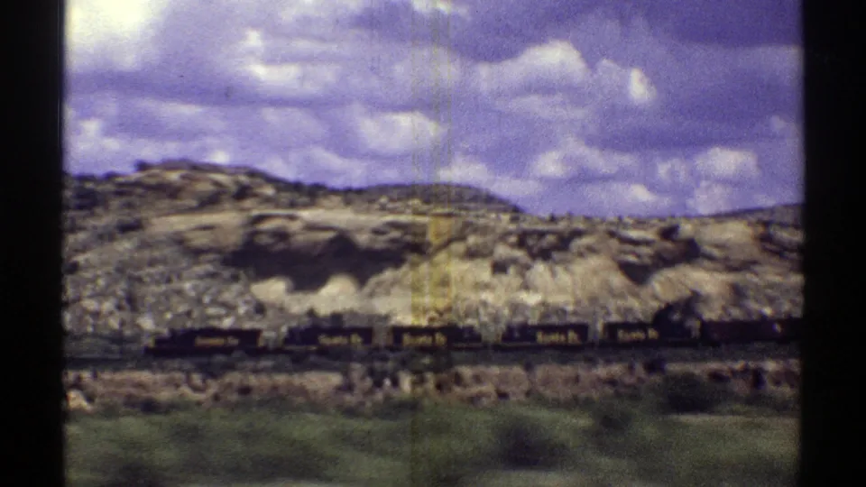 Vintage 8mm Arizona travel footage showing a distant train along rocky desert terrain, framed by vehicle-window edges and film wear.