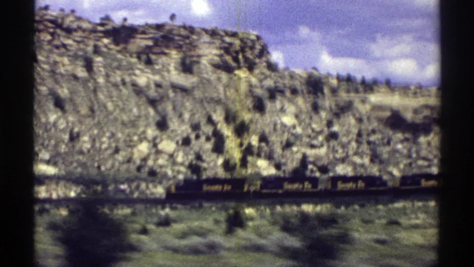 1969 Arizona 8mm frame showing Santa Fe freight cars moving past rocky hills and sparse desert vegetation.