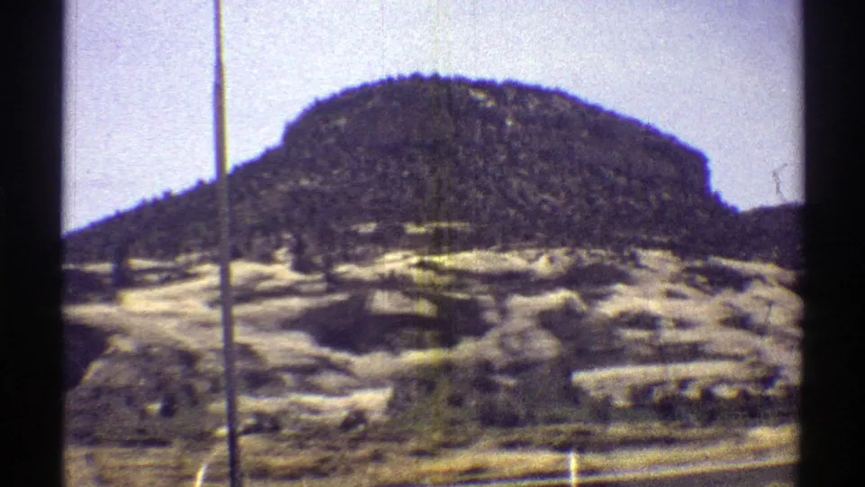 1969 Arizona 8mm view of a rounded rocky hill, pale arid ground, sparse vegetation, and a vertical window or pole line.