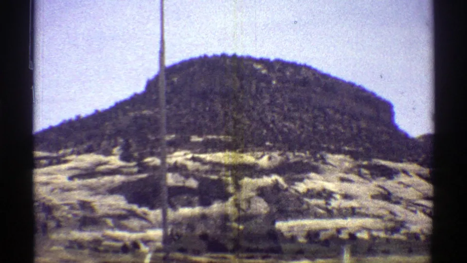1969 Arizona 8mm frame of a rocky desert hillside with scattered vegetation, seen from a passing train.