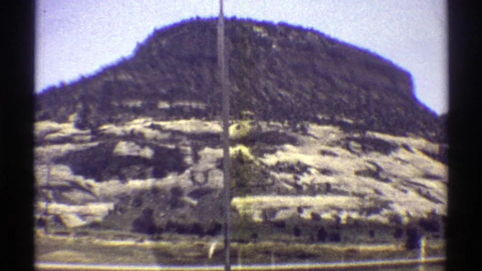 1969 Arizona 8mm view of a broad rocky hill with scrub, pale ground, and window-frame artifacts from train travel.