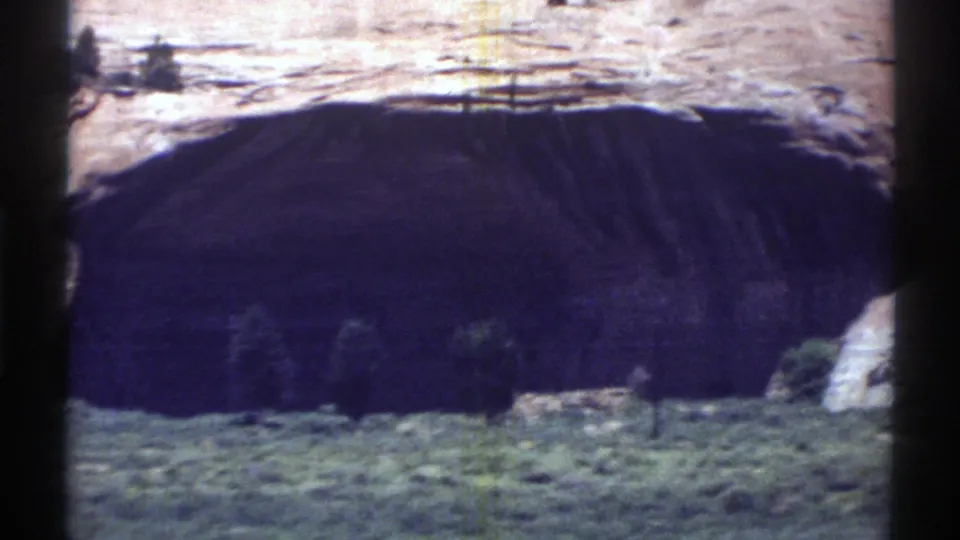1969 Arizona 8mm still showing the shadowed mouth of a sandstone arch or cave with scrub vegetation along the base.
