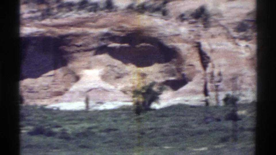 1969 Arizona 8mm frame passing beyond the main opening to a sunlit sandstone wall with a shadowed recess and sparse brush.