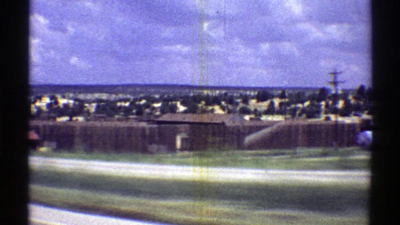 1969 Arizona roadside view with low buildings, open pavement, utility poles, and distant town edges.