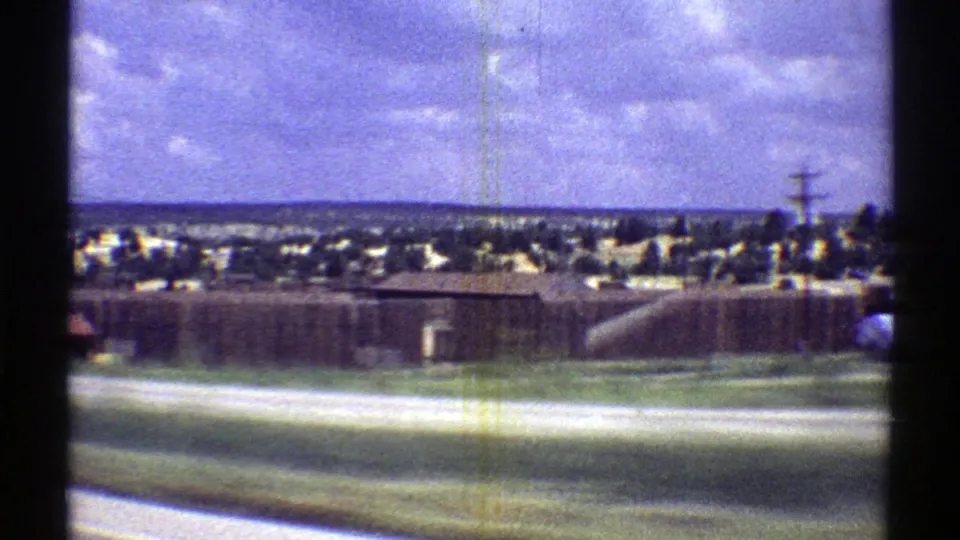 1969 Arizona roadside view with low buildings, open pavement, utility poles, and distant town edges.