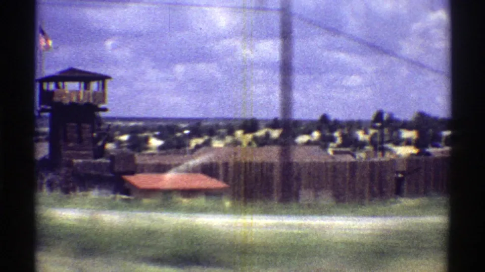 1969 Arizona drive-by view of a fenced roadside lot with a watchtower-like structure and low buildings beyond.
