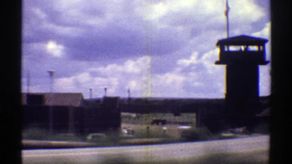 A roadside view of a prison tower, perimeter fencing, and institutional buildings in Arizona, captured on 8mm film in 1969.