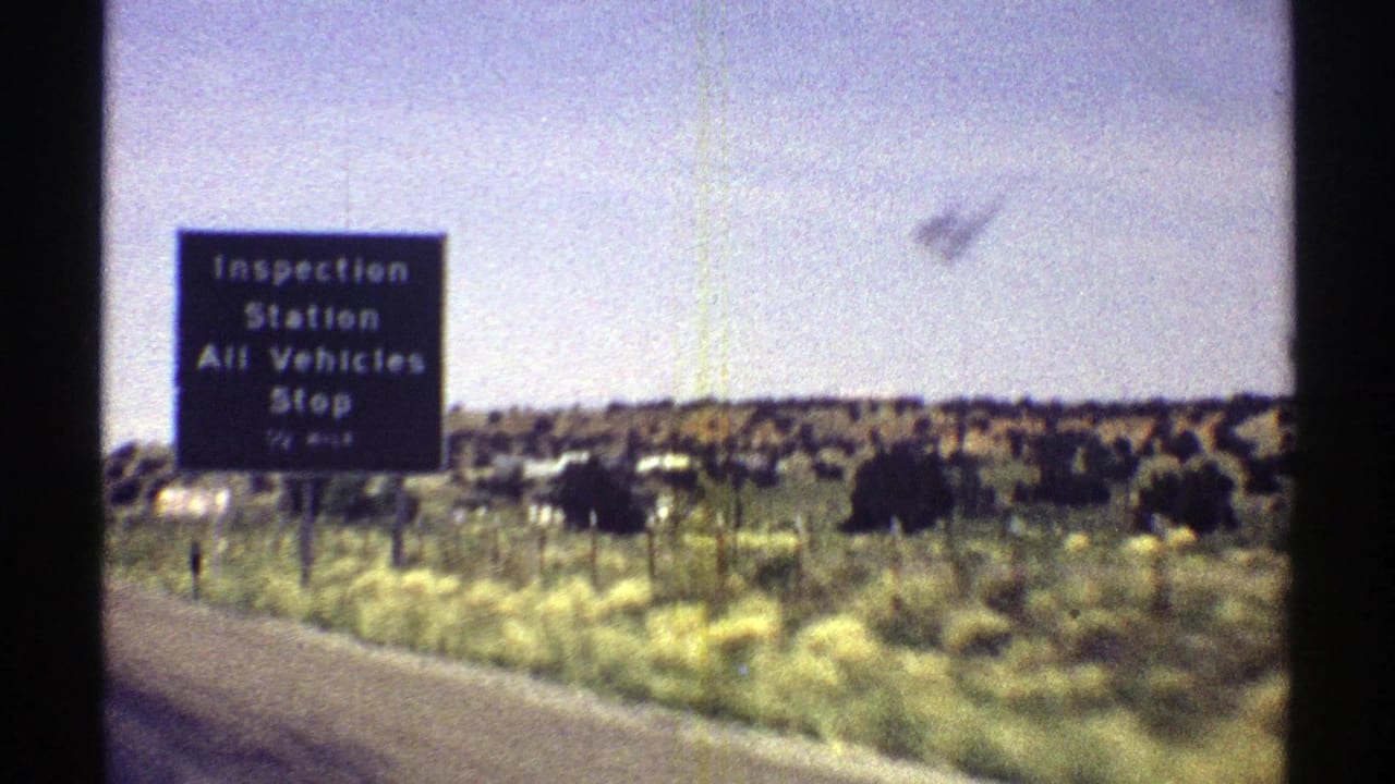 1969 Arizona 8mm frame showing a black inspection station sign beside an open desert highway landscape.