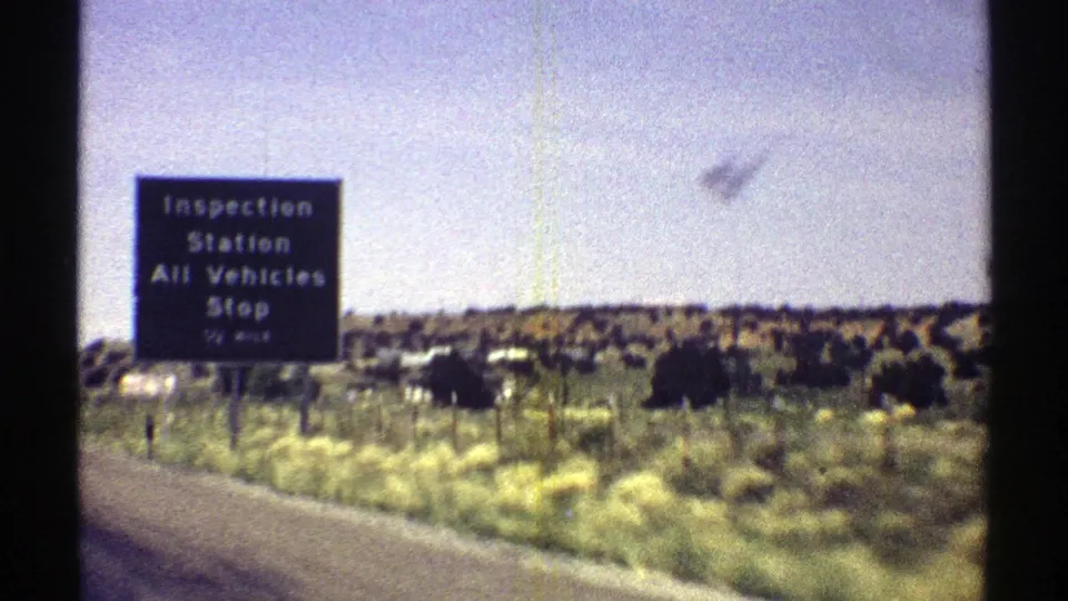 1969 Arizona 8mm frame showing a black inspection station sign beside an open desert highway landscape.