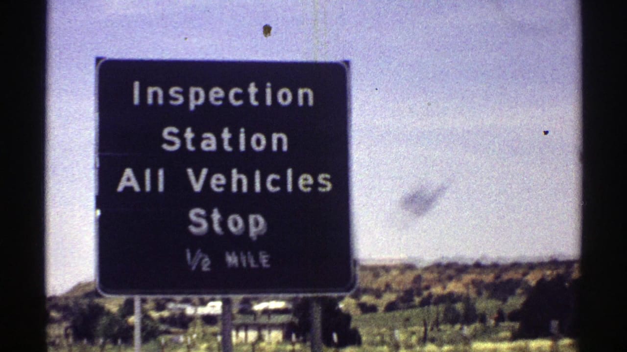 Close 1969 Arizona road-trip view of a black inspection station sign telling all vehicles to stop ahead.