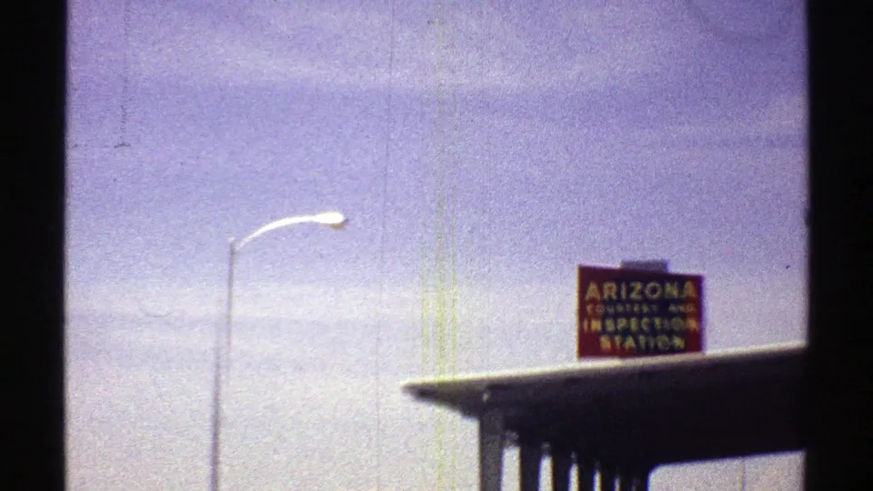 1969 Arizona 8mm frame showing a red state inspection station sign above a roadside canopy.