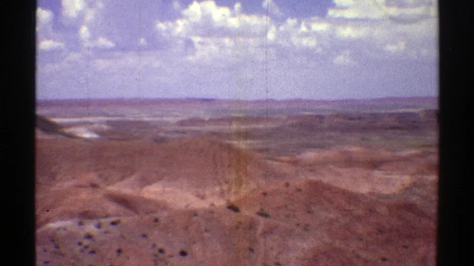 1969 Arizona home-movie frame of a broad desert vista with red rock terrain, dry washes, and far mesas.