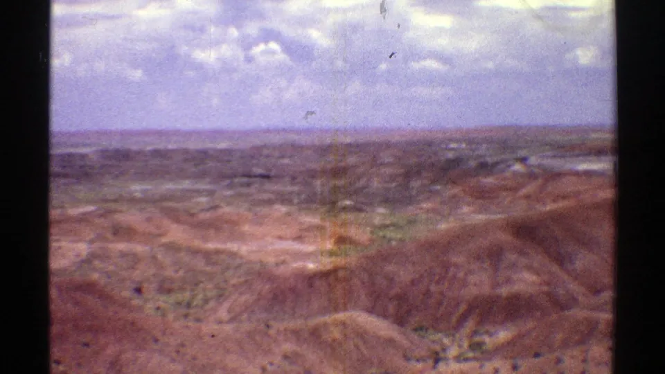 1969 Arizona 8mm frame showing rolling arid hills, patches of scrub, distant flatlands, and visible scratches in the film scan.