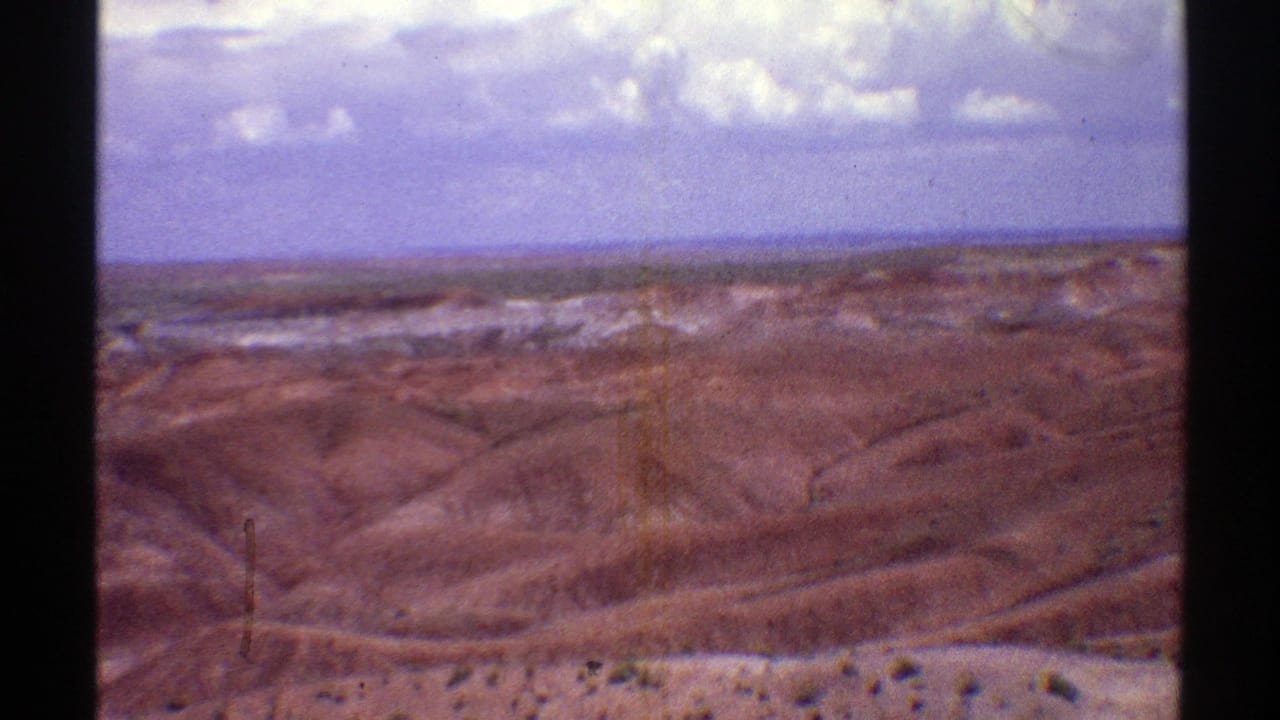 Rolling brown hills and pale ridges under a broad sky with white clouds.