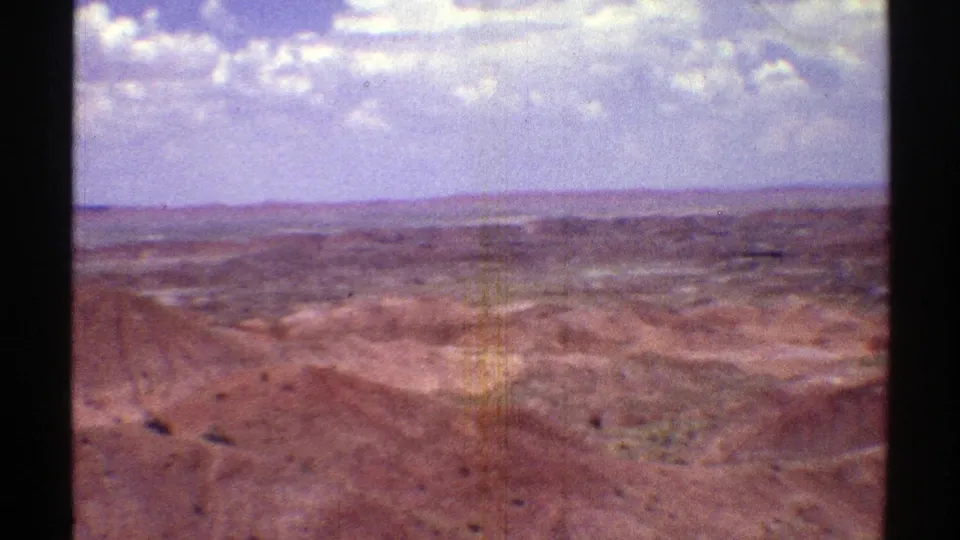 1969 Arizona 8mm view across low brown ridges and a wide desert basin, with pale sky and small clouds above.