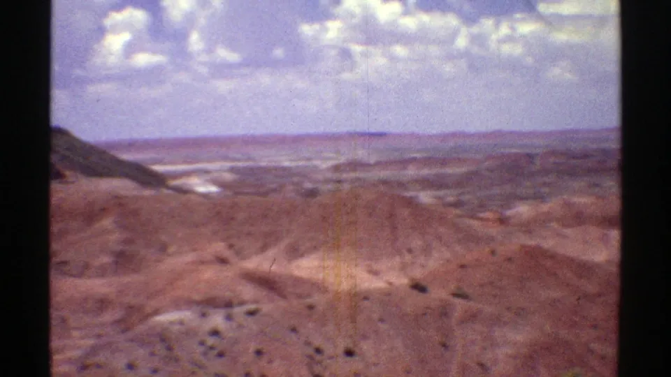 1969 Arizona frame showing brown desert hills, a darker hillside at left, sparse vegetation, and a bright distant horizon.