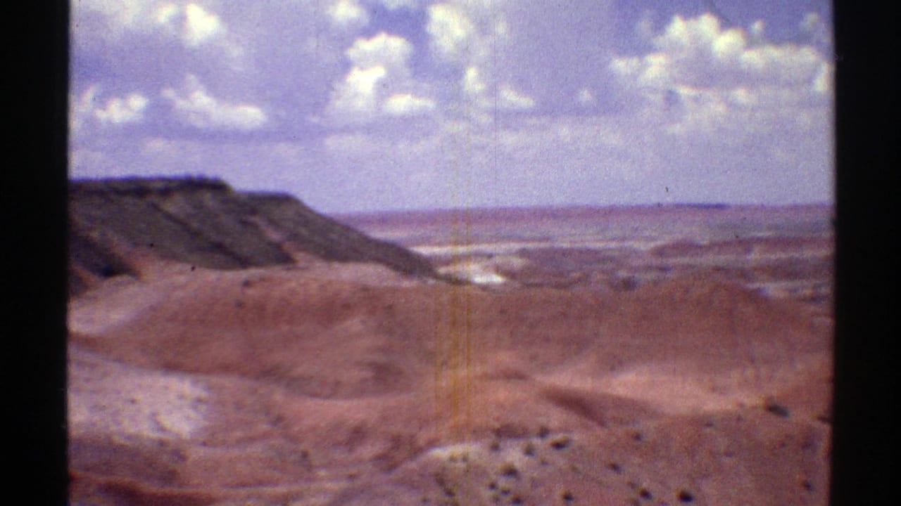 Reddish desert hills and rocky ridges beneath a blue sky with scattered clouds.