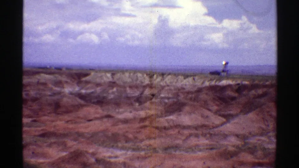 1969 Arizona desert view with rough foreground terrain, distant ridges, blue sky, and a small indistinct pale object on the horizon.