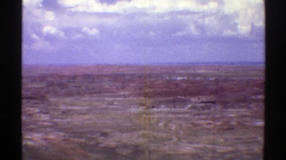 Faded 8mm aerial view of Arizona desert flats and low ridges, with a pale cloudy sky and visible vertical film marks.