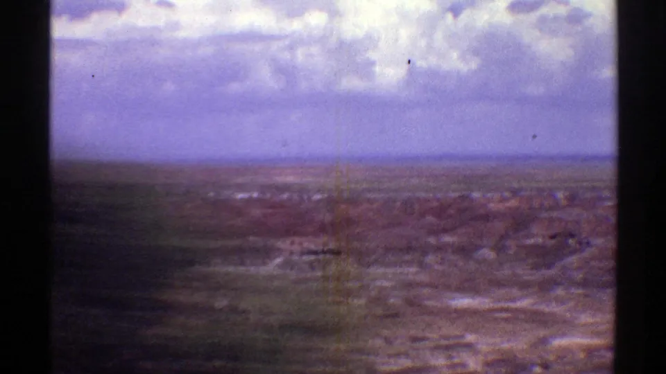 1969 Arizona aerial frame with red desert formations, distant plains, heavy clouds, and a dark film-edge shadow across the lower left.
