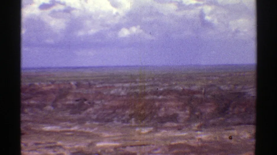 Color-shifted 8mm view across Arizona's arid terrain, with low fields or eroded ground stretching toward a distant horizon.
