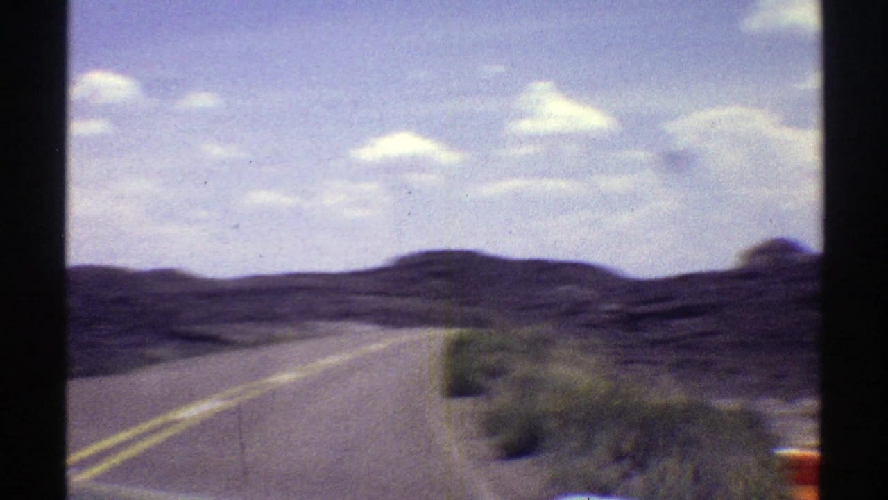 Two-lane desert road curving through low hills under a bright sky.