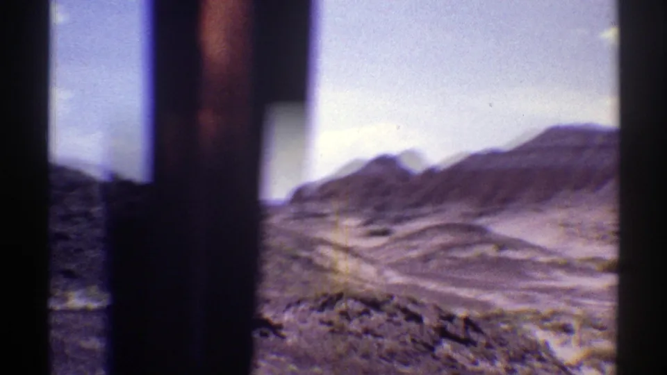Moving-car view of Arizona desert ridges, with a dark window edge and soft 8mm motion blur across the frame.