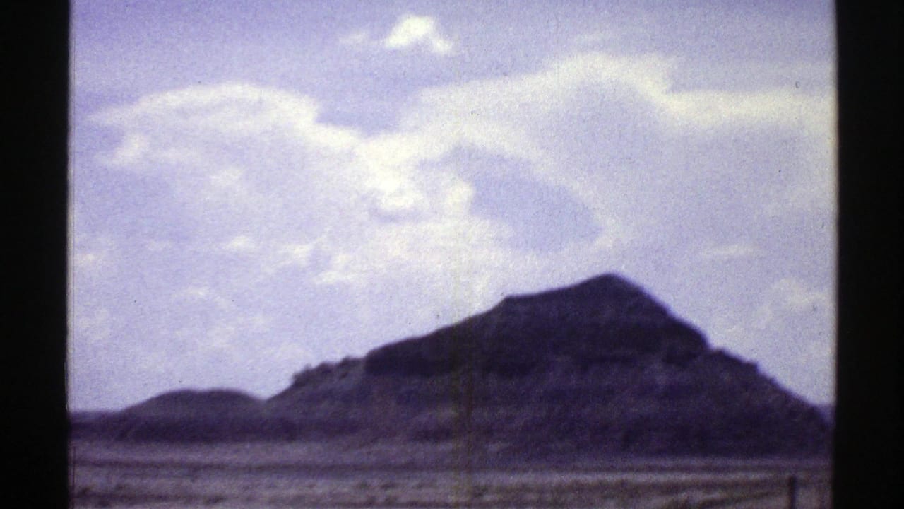 Rocky mountain peak under pale sky, seen through 8mm film gate edges.