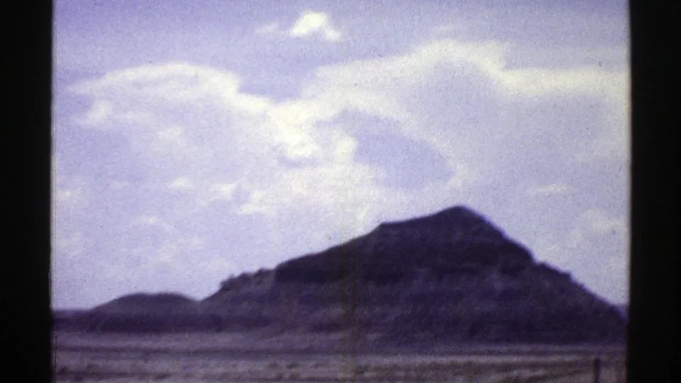 1969 Arizona home-movie frame showing a dark mountain peak across arid terrain beneath a pale blue sky.