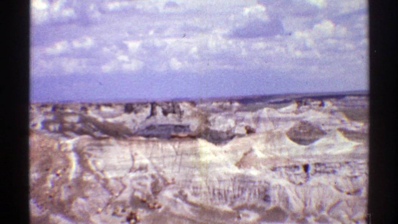 Distant pale desert hills and gullies beneath a blue sky with scattered clouds.