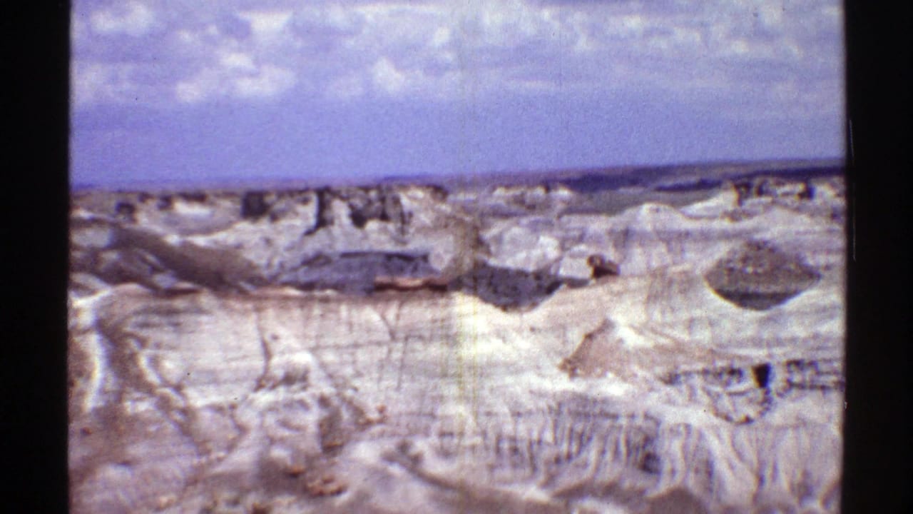Rocky desert badlands with layered ridges and scattered clouds overhead.