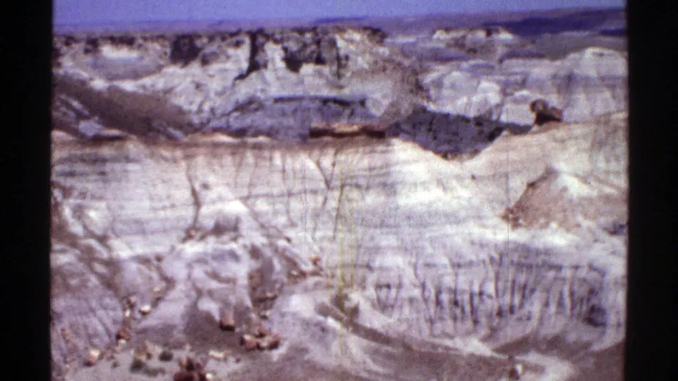 1969 Arizona 8mm frame with closer eroded rock faces, vertical gullies, dry slopes, and small stones in the foreground.