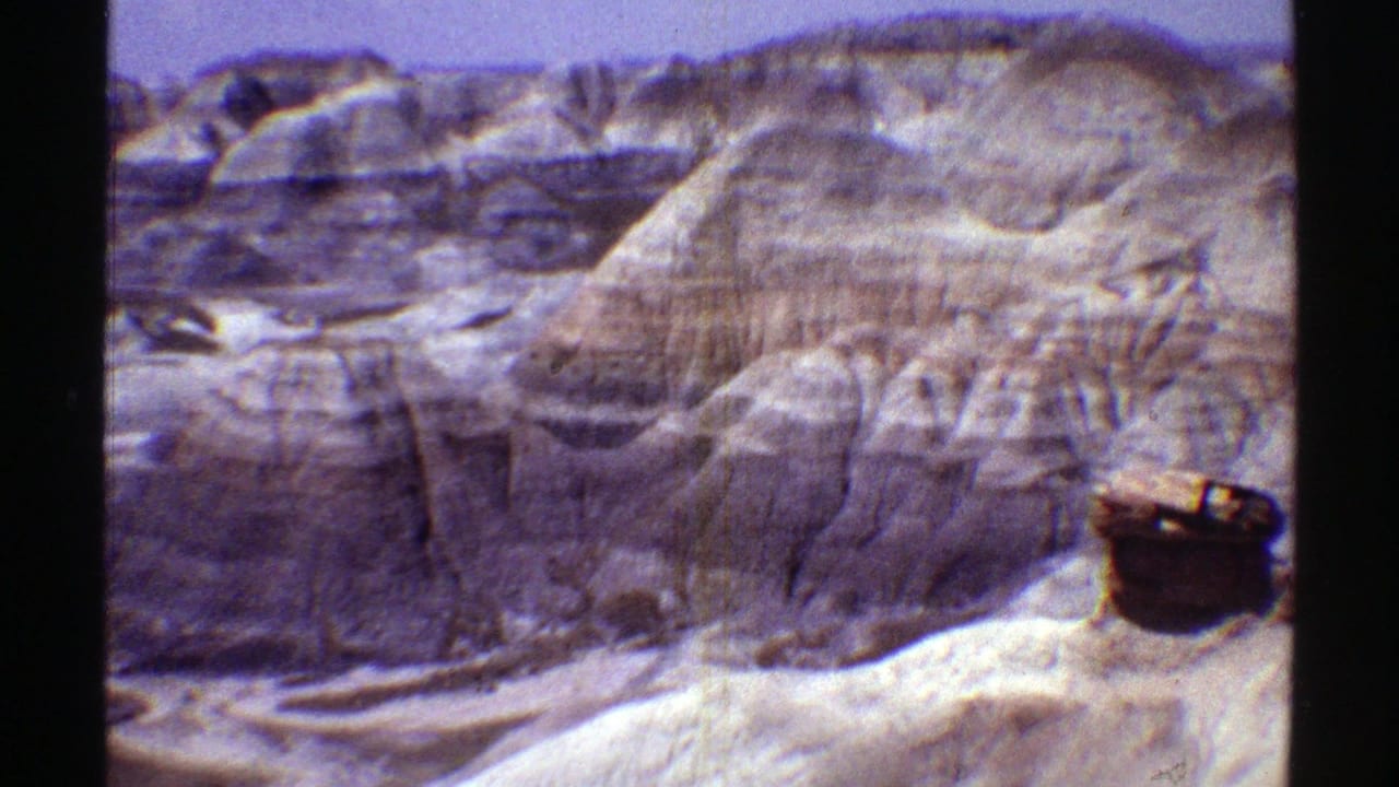 Layered desert cliffs with a dark barrel-like object in the foreground.