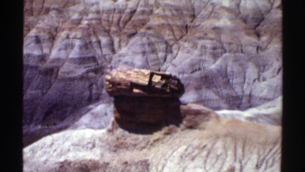 Arizona canyon view on 8mm film with a weathered pedestal-like rock form in front of eroded layered walls.