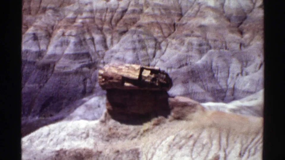Arizona canyon view on 8mm film with a weathered pedestal-like rock form in front of eroded layered walls.