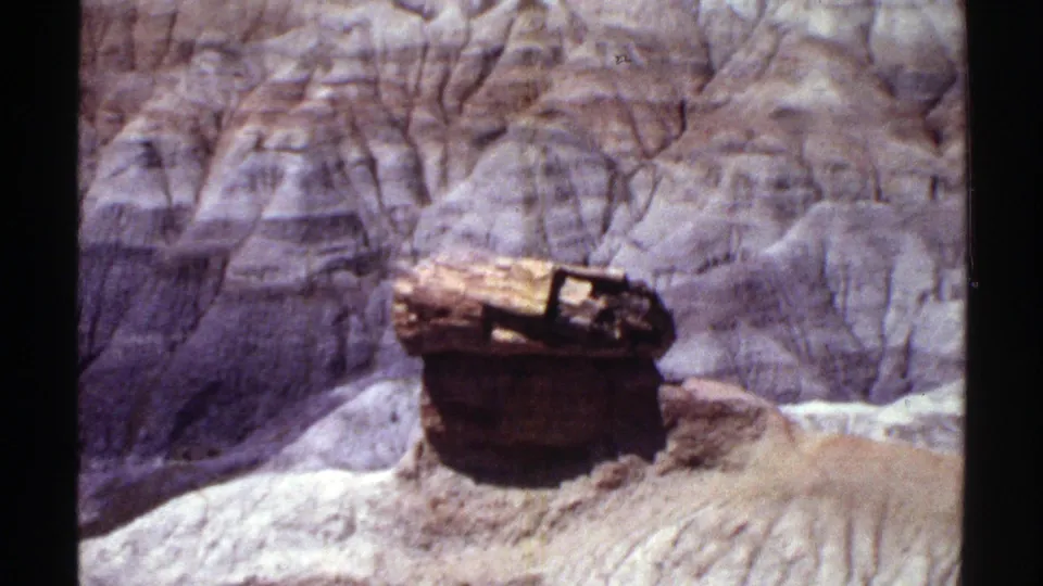 1969 Arizona home-movie frame with a closer look at a capped, rounded rock form on an eroded canyon slope.