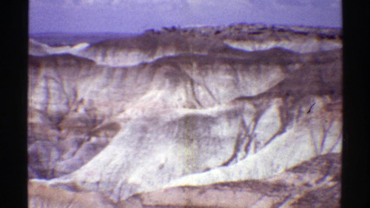 1969 Arizona 8mm frame of pale badlands and ridged desert cliffs seen from a tourist viewpoint.