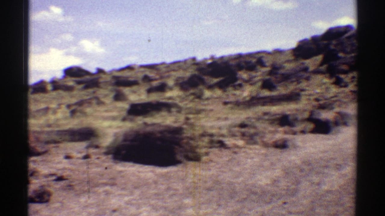 1969 Arizona 8mm frame of a rugged desert area dotted with petrified wood and small rocks.