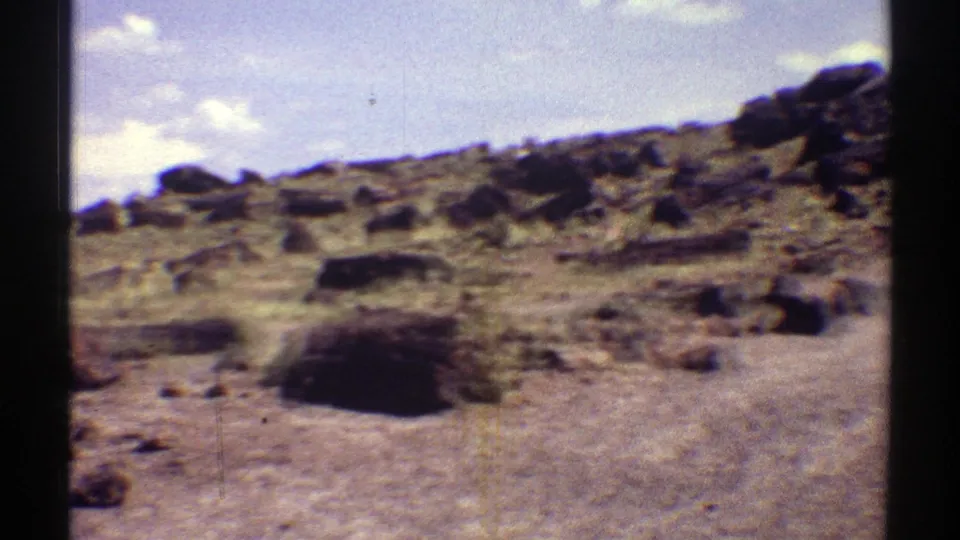 1969 Arizona 8mm frame of a rugged desert area dotted with petrified wood and small rocks.