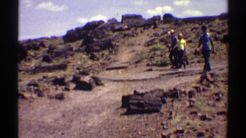 1969 Arizona 8mm frame showing three visitors walking along a dirt path among petrified wood and rocks.