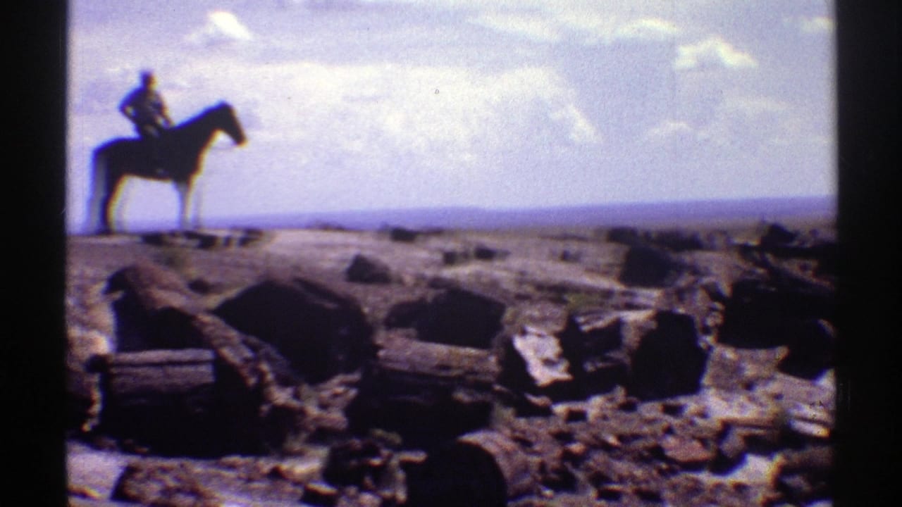 1969 Arizona 8mm frame showing a man on a dark horse against a hazy desert horizon, with scattered weathered logs and rocks below.