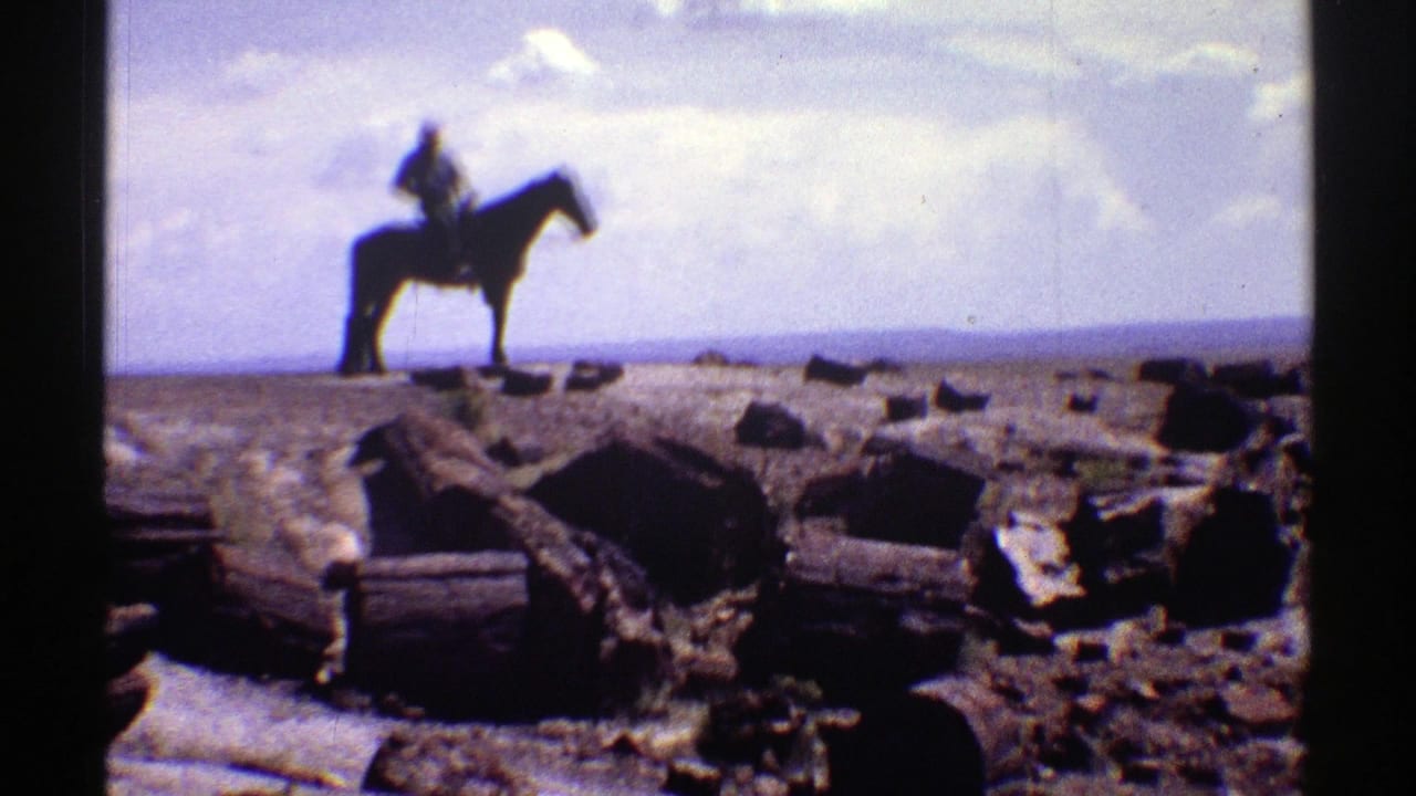 1969 Arizona desert view with a mounted rider silhouetted on the horizon above rough ground, logs, rocks, and a pale sky.