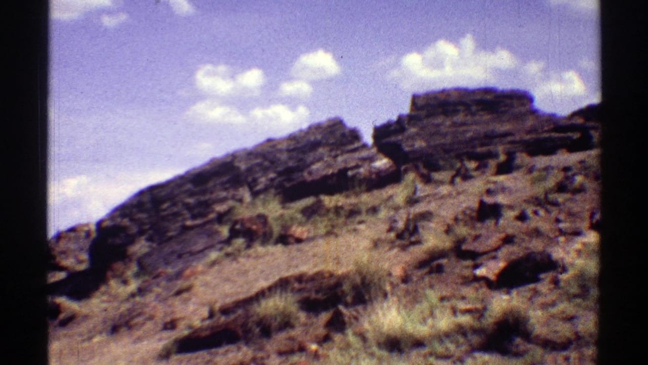 Rocky desert hillside with layered outcrops, dry grass, and blue sky.