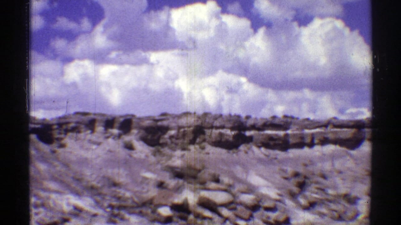 Rocky desert wash and low ridge beneath large white clouds.