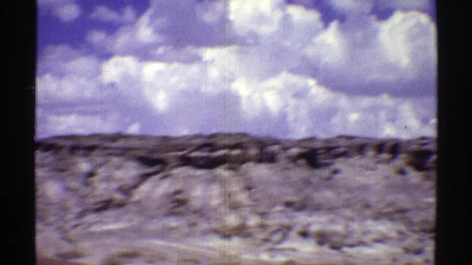 Soft 8mm view of a low Arizona desert ridge, scattered rocks, and expansive blue sky with white clouds.