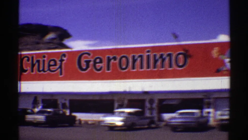 The Chief Geronimo sign fills the frame above parked mid-century cars at an Arizona roadside stop.