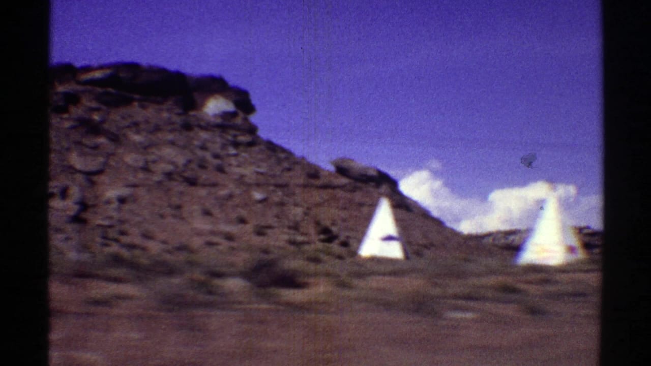 White teepees with red markings beside a rocky desert hillside.